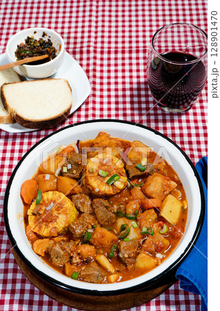 Hearty beef stew called carbonada simmering with vegetables and corn on the cob, served with bread and wine Hearty beef stew called carbonada simmering with vegetables and corn on the cob, served with bread and wine 128901470