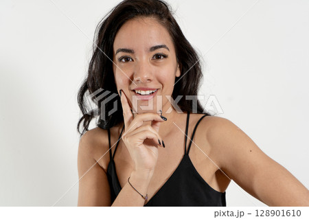 Young latin woman touching face and smiling gently on white background 128901610