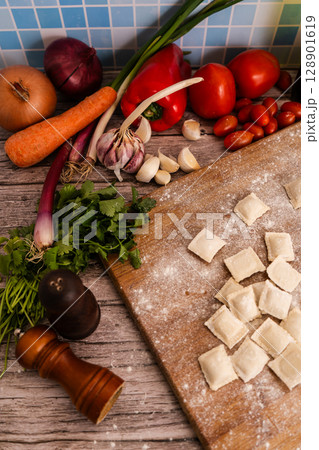 Fresh ravioli with flour on wooden cutting board with vegetables and spices. Vertical Orientation Fresh ravioli with flour on wooden cutting board with vegetables and spices. Vertical Orientation 128901619