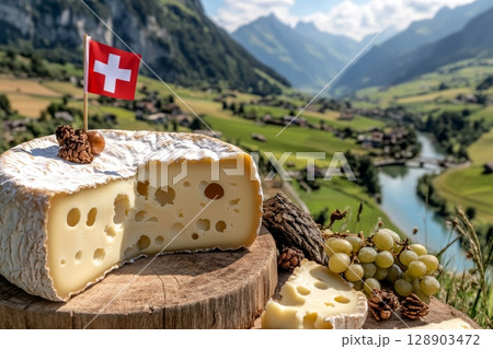 Swiss cheese wheel with swiss flag, grapes, and nuts overlooking picturesque valley 128903472