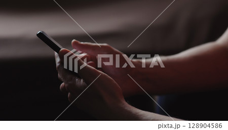 Closeup young man in black t-shirt typing messages on smartphone working from home side view 128904586