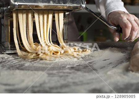 Caucasian female hands making fettuccine noodles using mechanical pasta machine Caucasian female hands making fettuccine noodles using mechanical pasta machine 128905005