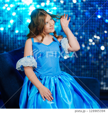 Cute teenage girl in blue doll dress posing against sequin wall background 128905394