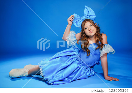 Cute teenage girl in blue doll dress with big blue bow posing lying on the floor 128905395