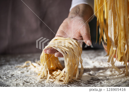 Caucasian female hands holding raw fettuccine noodles after drying 128905416