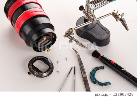 A broken lens of a professional camera and repair tools on a white table.  128905429