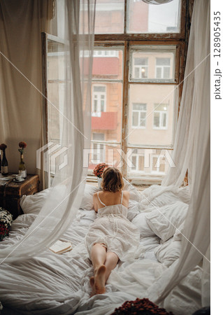 a young blonde woman in a white dress on white sheets 128905435