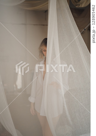 An attractive woman in a white shirt on a nude barely in tulle from the window. 128905462