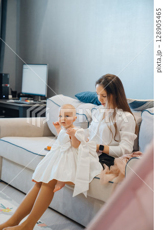 Cute baby daughter in an elegant dress lies on her mother's knees Cute baby daughter in an elegant dress lies on her mother's knees 128905465