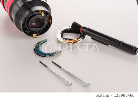 A broken lens of a professional camera and repair tools on a white table.  128905466