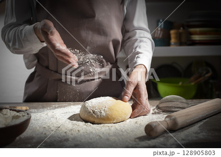 Baking concept. Caucasian female hands throwing flour at the dough. 128905803