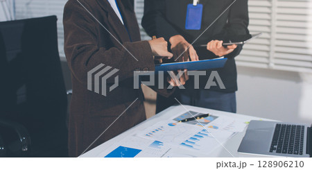 Focused young businessman signing agreement with skilled lawyer in eyeglasses. Concentrated financial advisor showing place for signature on paper contract document to male client at meeting in office 128906210