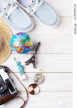 Travel planning simple background of compass, film camera, straw hat, moccasins, globe and souvenirs on white planks flat lay with copy-space 128906516