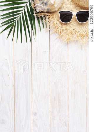 Vacation travel planning simple background of straw hat sunglasses palm leaves and shell on white planks flat lay with copy-space 128906766