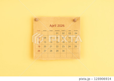 April 2026 brown calendar with wooden thumbtack on yellow color background. 128906914