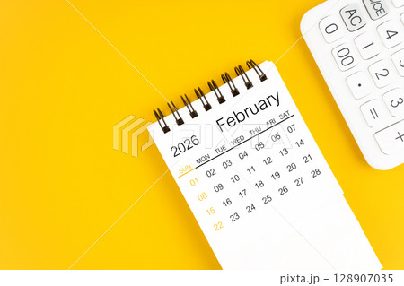 February 2026 calendar and calculator on yellow background, Flat lay. February 2026 calendar and calculator on yellow background, Flat lay. 128907035