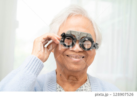 Optometrist checking Asian elderly woman ophthalmic vision eye test and using optical trial frame. 128907526