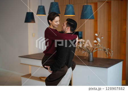 Couple joyfully embracing each other in a cozy modern kitchen setting Couple joyfully embracing each other in a cozy modern kitchen setting 128907882