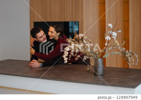 Couple enjoying intimate moment in modern kitchen with floral arrangement Couple enjoying intimate moment in modern kitchen with floral arrangement 128907949