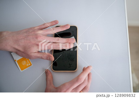 Man cleaning smartphone screen with dry wipe before applying screen protector 128909832