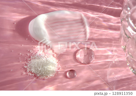 Beauty products on a pink background with highlights from the water. 128911350