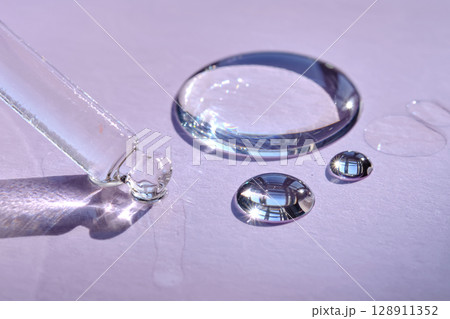 A drop of serum with a pipette on a purple background. A drop of serum with a pipette on a purple background. 128911352