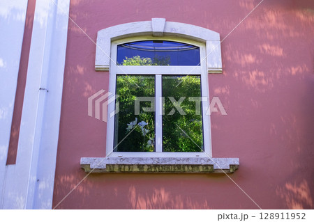 Window with white frame on a pink building exterior with decorative trim. 128911952