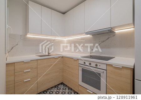 Modern kitchen with white cabinets and wooden accents. Features a marble backsplash, stainless steel appliances, and patterned floor tiles. Modern kitchen with white cabinets and wooden accents. Features a marble backsplash, stainless steel appliances, and patterned floor tiles. 128911961