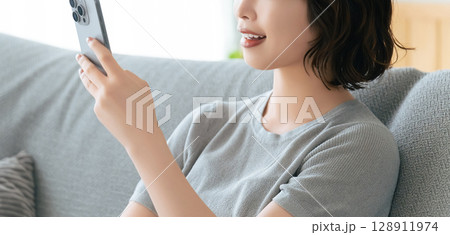 ソファに座ってスマートフォンを使う笑顔の女性 128911974