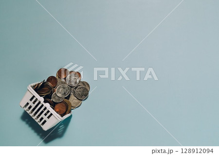 Mini Shopping Basket Full of Coins on Blue Background Mini Shopping Basket Full of Coins on Blue Background 128912094
