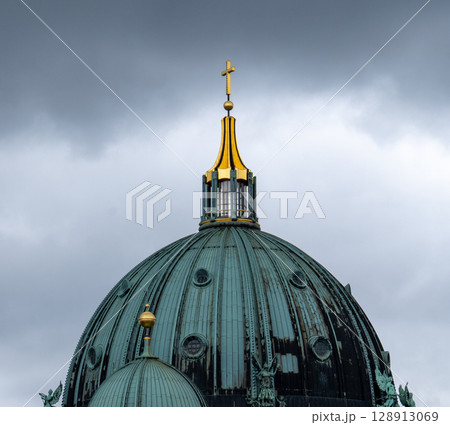 Berlin. Germany. 07.26.2025 The majestic dome of the Berlin Cathedral with a golden cross against the backdrop of a cloudy sky. 128913069