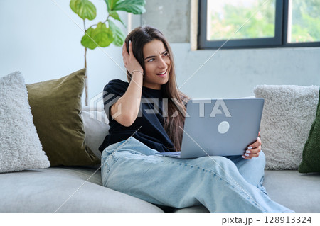 Young teenage girl using laptop for video chat sitting on sofa at home Young teenage girl using laptop for video chat sitting on sofa at home 128913324