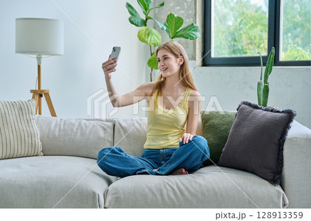 Smiling young teenage female taking selfie photo on smartphone 128913359