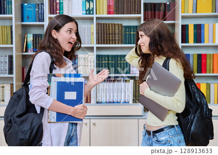Two teenage students classmates chatting standing in classroom library Two teenage students classmates chatting standing in classroom library 128913633