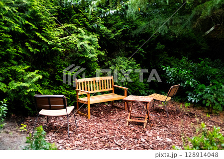 Wooden garden furniture amidst lush greenery in tranquil outdoor setting Wooden garden furniture amidst lush greenery in tranquil outdoor setting 128914048
