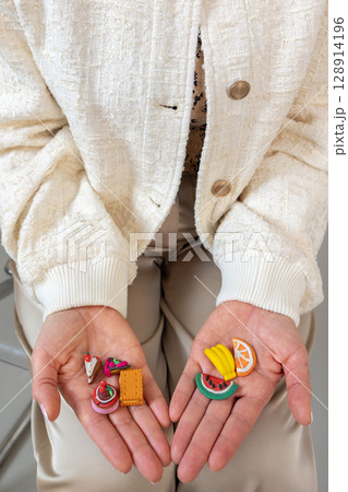 Female palms close-up with miniatures of harmful and healthy food. Small figures of cake, cookies, sweets, fruits. Concept of healthy lifestyle and proper nutrition. Vertical photo. High quality photo 128914196