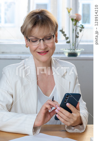 Portrait of business woman. Confident mature woman using mobile phone and typing. Vertical photo. High quality photo 128914210
