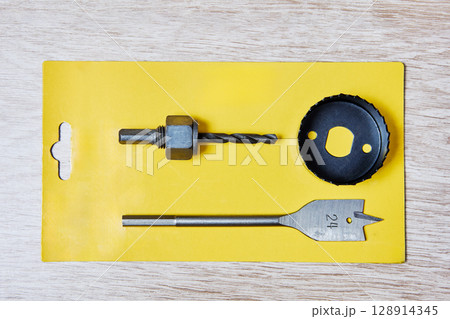 Set of woodworking tools including spade bit hole saw arbor and saw blade arranged on yellow card packaging for DIY drilling and construction tasks. 128914345