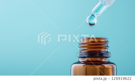 Dropper releasing droplet into amber glass bottle against blue background 128919622