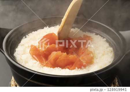湯気の立つ土鍋で炊いた丸ごとトマトの炊き込みご飯をチーズを加え木べらで混ぜる 湯気の立つ土鍋で炊いた丸ごとトマトの炊き込みご飯をチーズを加え木べらで混ぜる 128919941