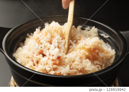 湯気の立つ土鍋で炊いた丸ごとトマトの炊き込みご飯をチーズを加え木べらで混ぜる 128919942