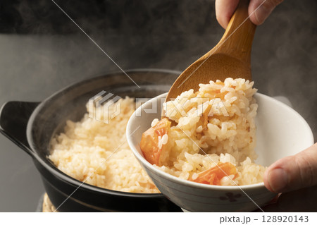 湯気の立つ土鍋で炊いた丸ごとトマトの炊き込みご飯を茶碗にしゃもじで盛り付ける 128920143