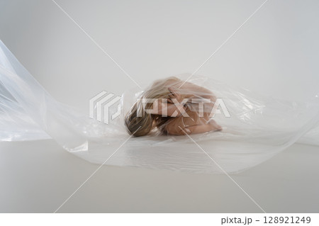 Studio portrait of a beauty with blonde hair wrapped in transparent material Studio portrait of a beauty with blonde hair wrapped in transparent material 128921249