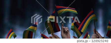 Mauritius flags in their hands on a blurred urban background Mauritius flags in their hands on a blurred urban background 128923240