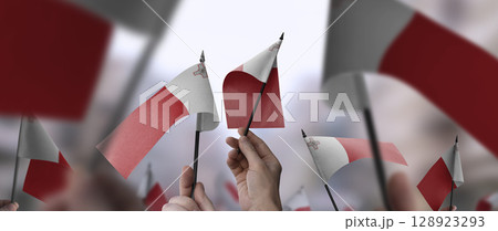Malta flags in their hands on a blurred urban background Malta flags in their hands on a blurred urban background 128923293