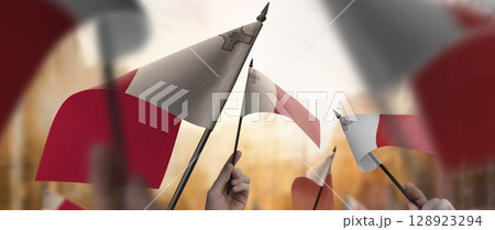 Malta flags in their hands on a blurred urban background 128923294