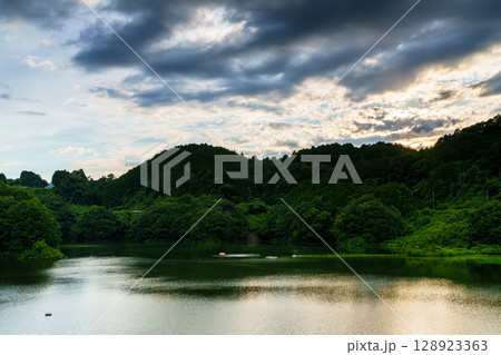 上空雲に覆われた奈良布目ダムで対岸の山際に沈んで行く夕日⑤ 128923363