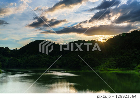 上空雲に覆われた奈良布目ダムで対岸の山際に沈んで行く夕日➅ 128923364