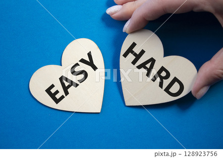 Easy or Hard symbol. Concept word Easy or Hard on wooden hearts. Businessman hand. Beautiful blue background. Business and Easy or Hard concept. Copy space Easy or Hard symbol. Concept word Easy or Hard on wooden hearts. Businessman hand. Beautiful blue background. Business and Easy or Hard concept. Copy space 128923756