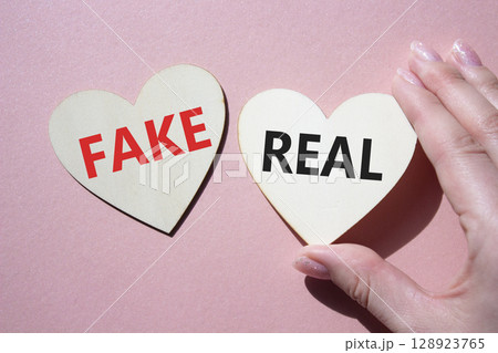 Real or Fake symbol. Concept word Real or Fake on wooden hearts. Beautiful pink background. Business and Real or Fake concept. Copy space Real or Fake symbol. Concept word Real or Fake on wooden hearts. Beautiful pink background. Business and Real or Fake concept. Copy space 128923765